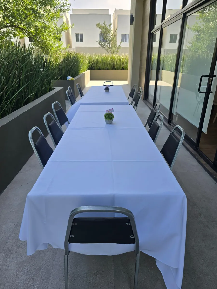 Mesa rectangular con mantel blanco y sillas plegables acojinadas en terraza